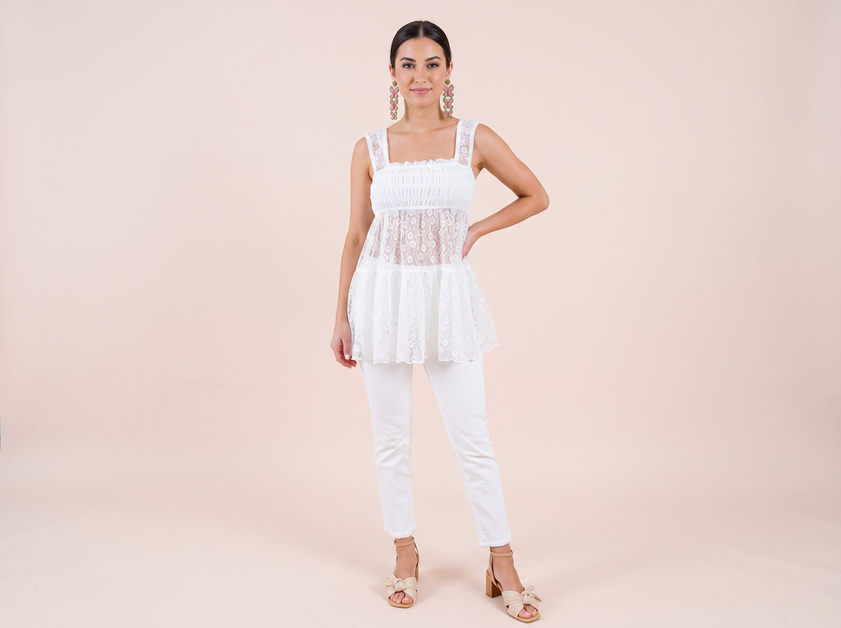 Woman wearing pink and green beaded butterfly earrings, a white lace smocked top, white cropped jeans and beige bow block-heel sandals