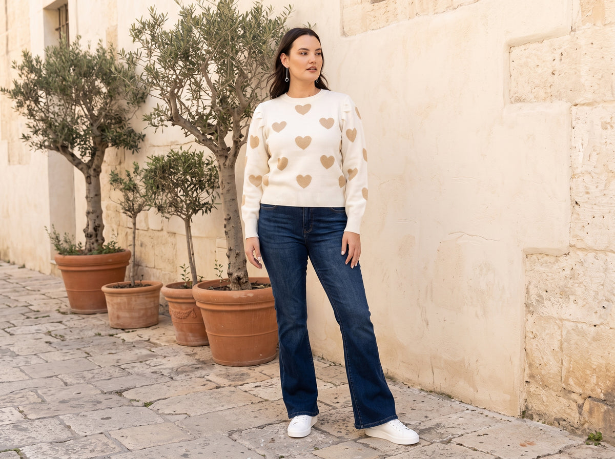 Woman wearing slim heart drop earrings, a heart print sweater, blue flare jeans and white glitter-star sneakers