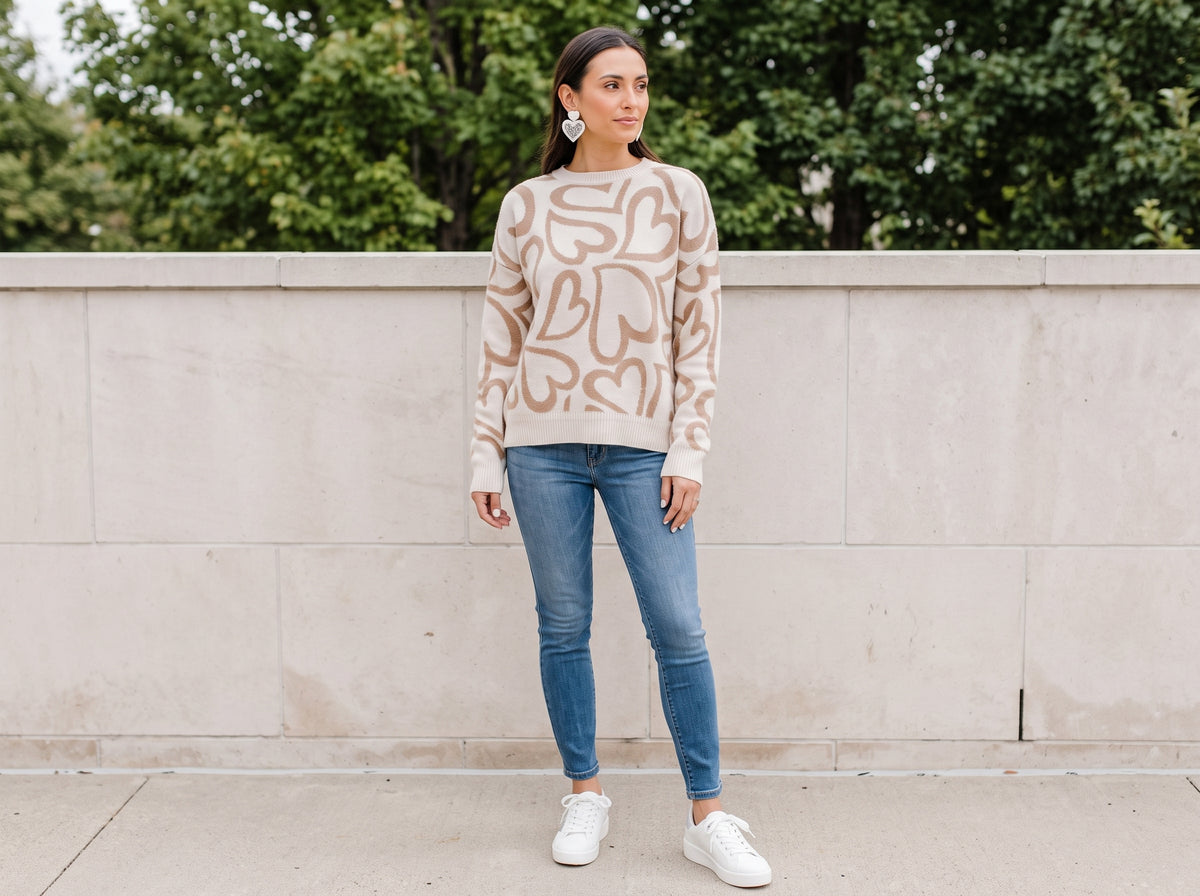 Woman wearing white beaded double-heart earrings, a mocha heart sweater, blue skinny jeans and white glitter-star sneakers