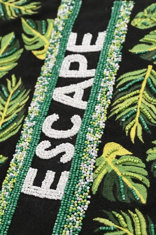 A tropical-themed tote bag featuring green leaf embroidery, sequin "ESCAPE" lettering, fabric-wrapped handles, and a detachable crossbody strap.