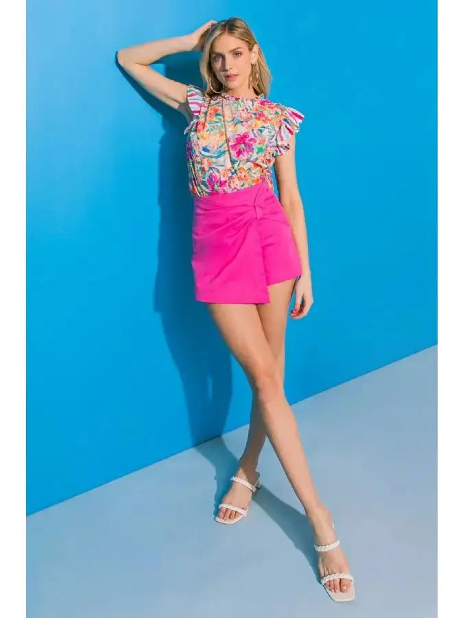 Model wearing a floral ruffle sleeve high neck top with vibrant colors against a blue background.