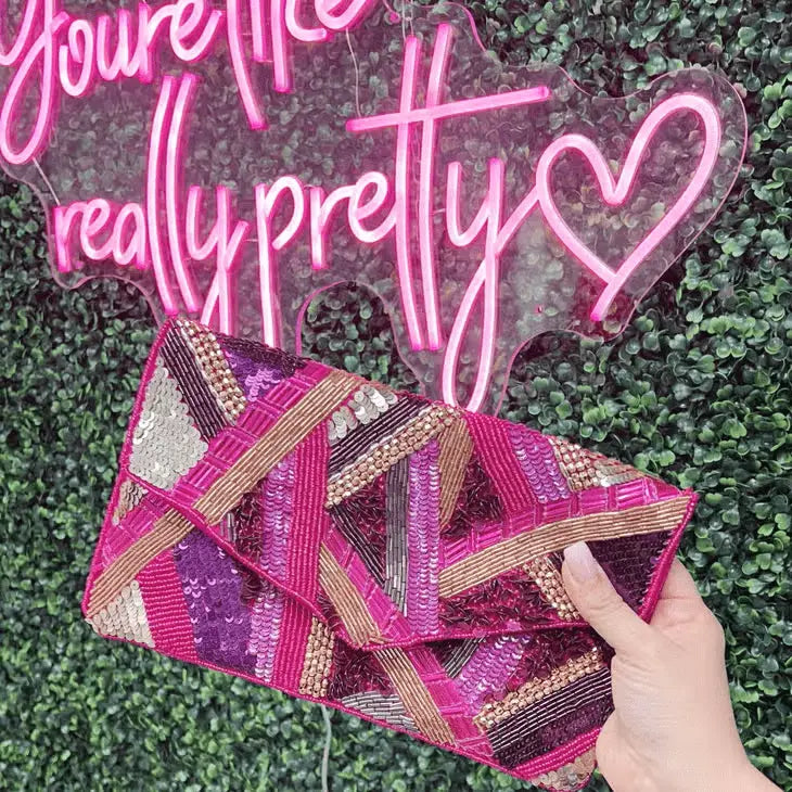 A dazzling fuchsia and gold hand-beaded clutch with intricate sequin details, featuring an envelope design and a gold-tone chain strap for versatile styling.