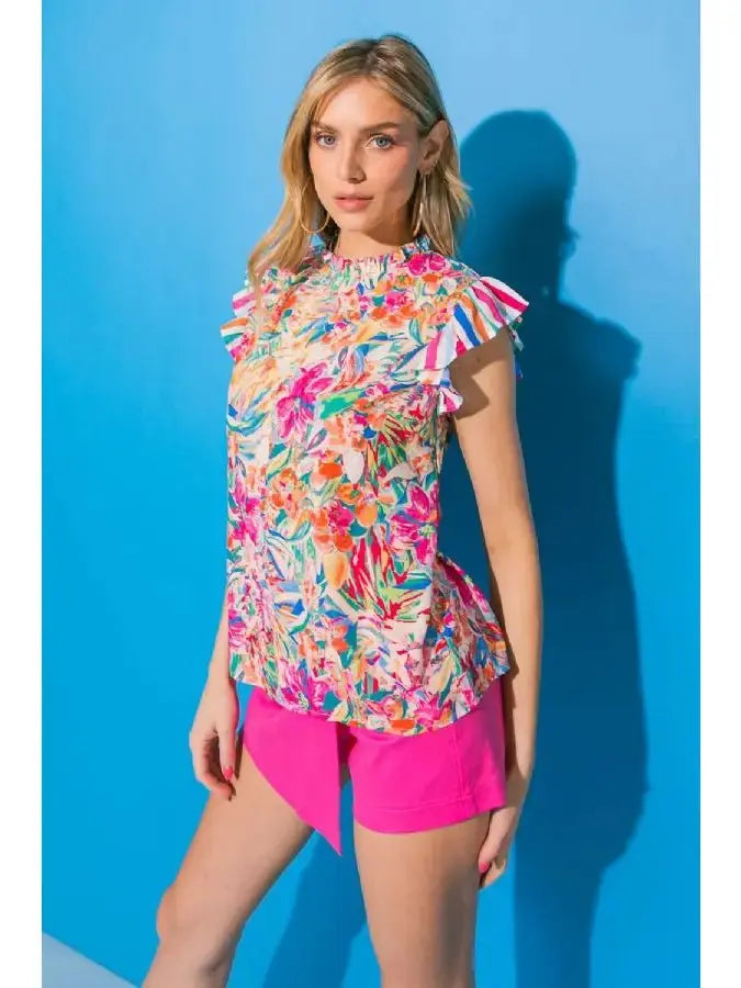 Model wearing a floral ruffle sleeve high neck top with vibrant colors against a blue background.