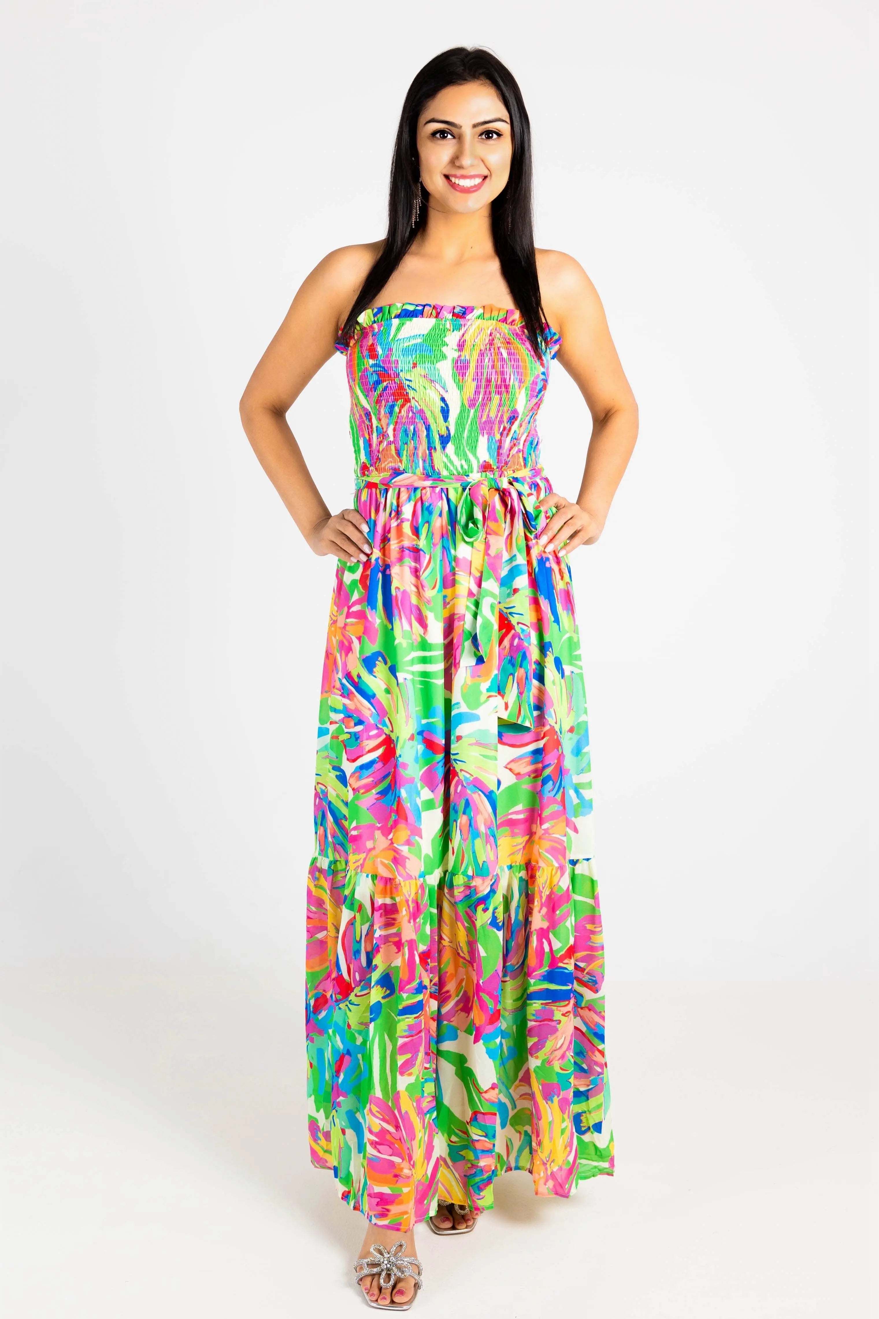 A woman wearing a vibrant tropical-print strapless maxi dress with a smocked bodice and flowy tiered skirt, perfect for summer vacations.