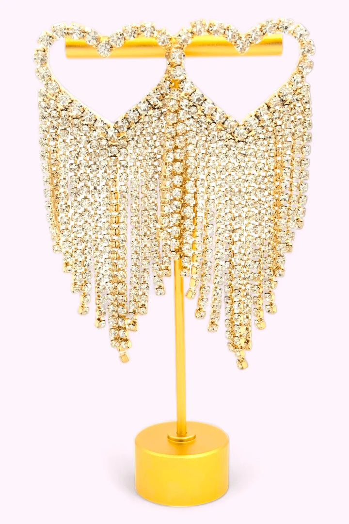 Woman wearing radiant heart fringe rhinestone earrings with cascading rhinestones, styled with an off-shoulder pink dress.
