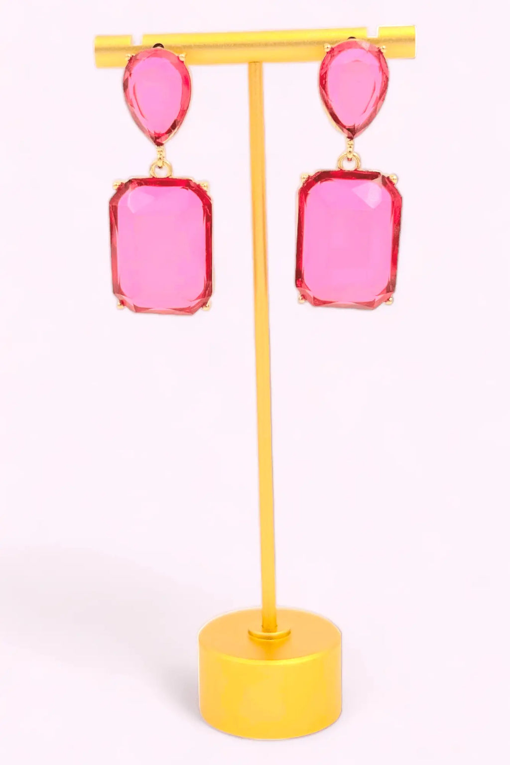 Bold pink gemstone statement drop earrings with gold-plated metal setting displayed on a jewelry stand.