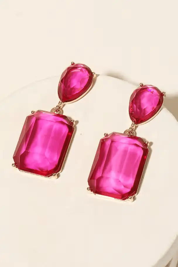 Bold pink gemstone statement drop earrings with gold-plated metal setting displayed on a jewelry stand.