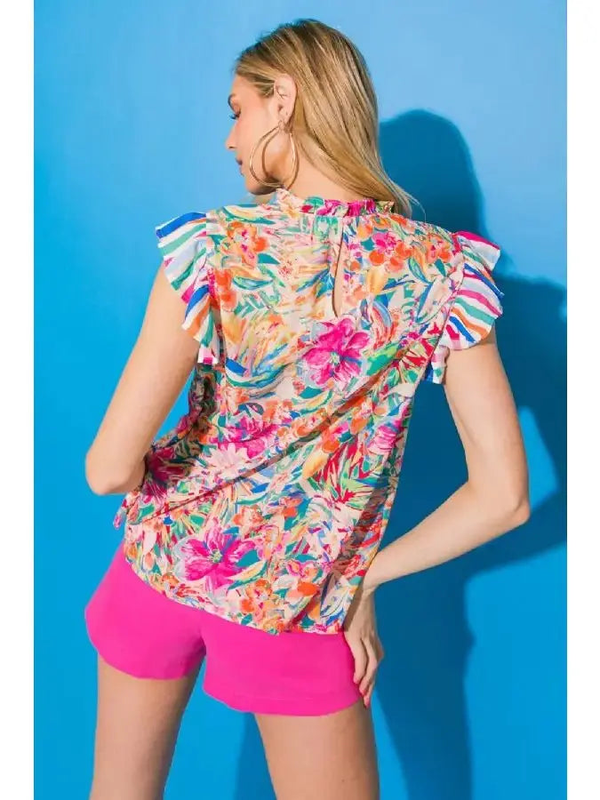 Model wearing a floral ruffle sleeve high neck top with vibrant colors against a blue background.